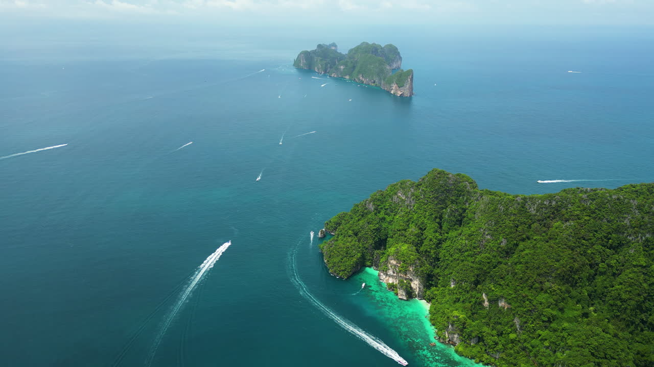Bird's eye view aerial above rugged tropical forested island as boats speed through ocean to offshore isolated spot