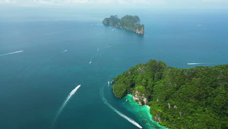 bird's eye view aerial above rugged tropical forested island as boats speed through ocean to offshore isolated spot
