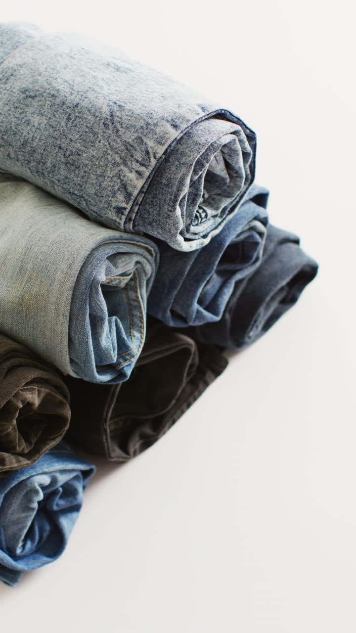 Vertical video of folded jeans with different shades on white background with copy space