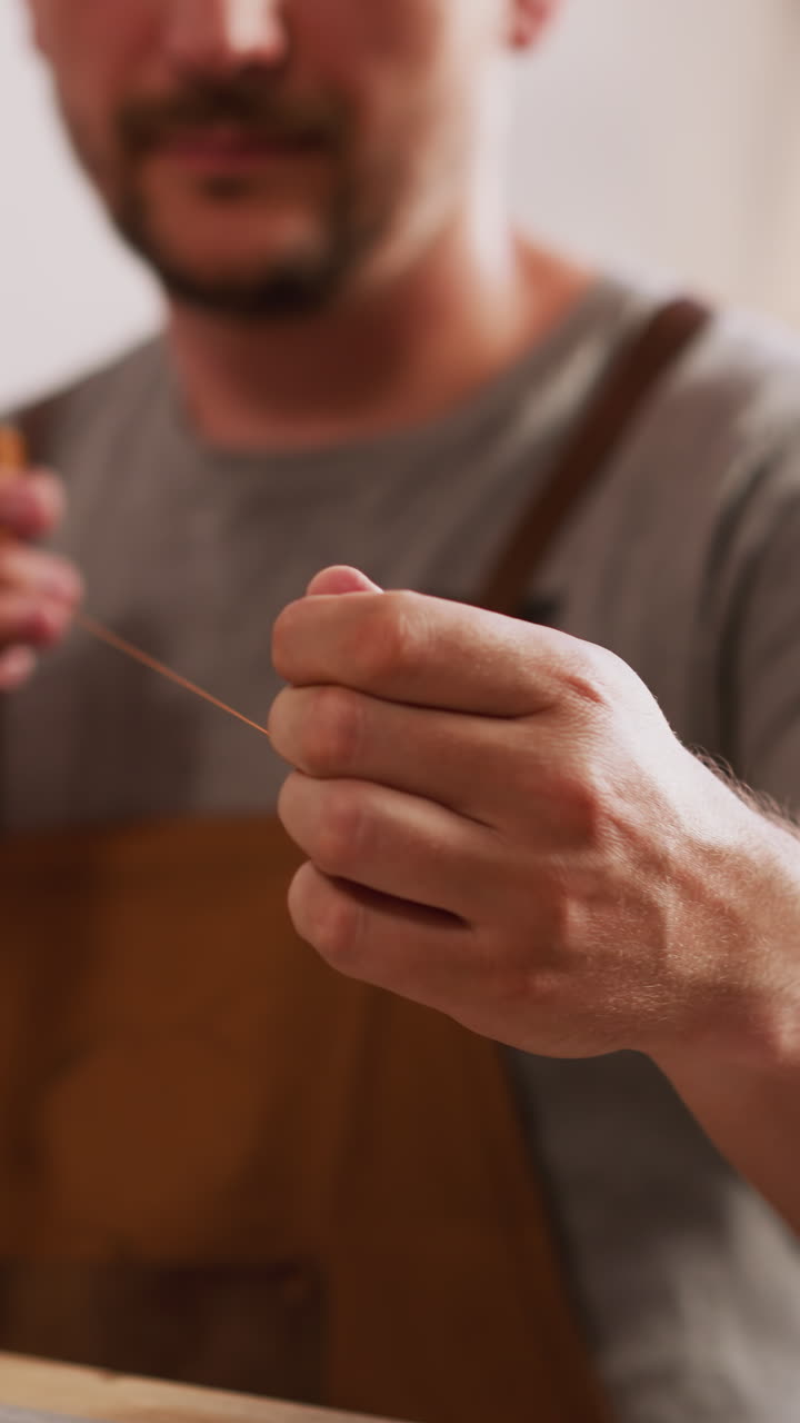 Worker pulls waxed thread for leather materials sewing in workshop closeup. Manual tools for handcraft. Accessories manufacturing process