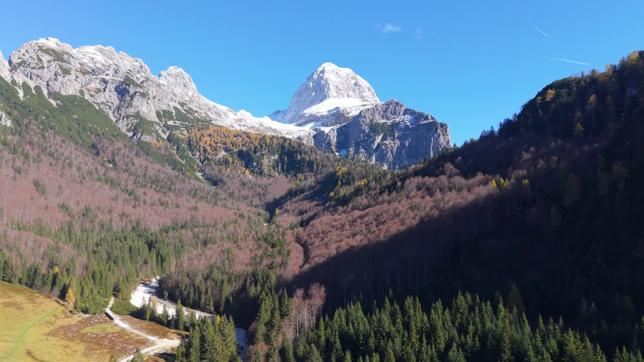 Julian Alps aerial flight with snow mountains and autumn forest