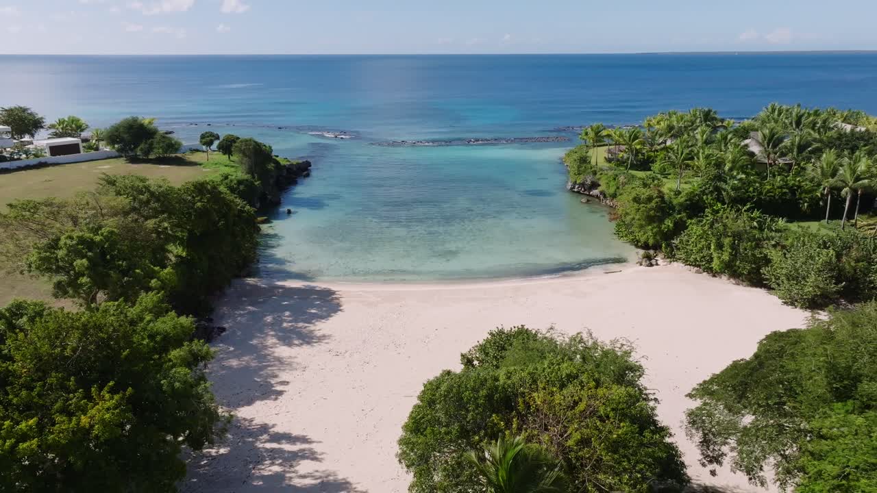 Backward flyover tropical vegetation and white sand Caleton beach in the Dominican Republic. Panoramic aerial of beach bay with coral reefs
