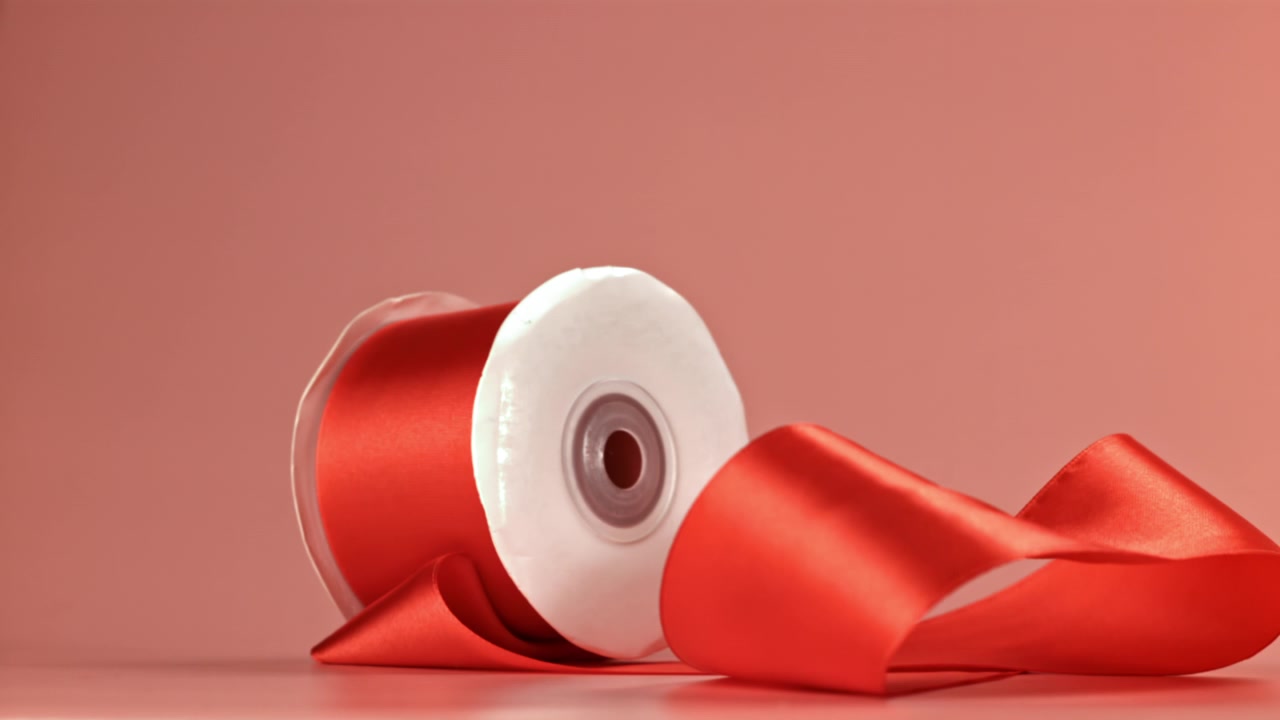 Red Ribbon Spool Falling and Unwinding on Pink Background
