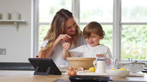 madre e hijo en pijama horneando en la cocina en casa siguiendo la receta en una tableta digital
