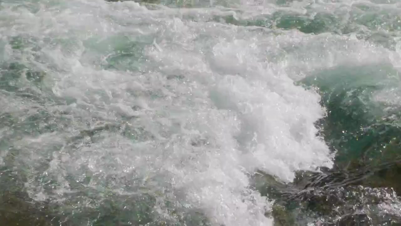 River water current foam splash, gimbal stabilizer shot. Tight macro close up tracking white bubbles forming from powerful blue mountain rapids stream.