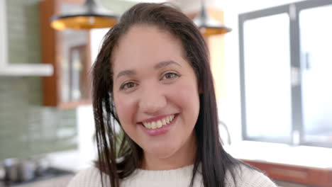 Happy-biracial-woman-with-straight-hair-standing-and-smiling-in-sunny-kitchen