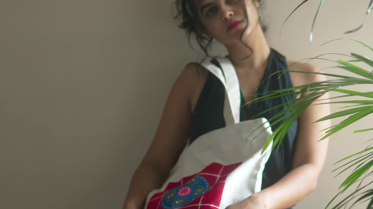 Mujer posando con un bolso de lona con estampado personalizado, celebrando la moda casual y las tendencias de accesorios sostenibles en un ambiente interior relajado.