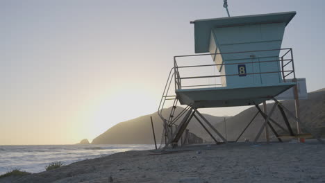 panning shot of lifeguard tower at an empty mondo's beach as the sun sets behind a distant mountain located in southern california