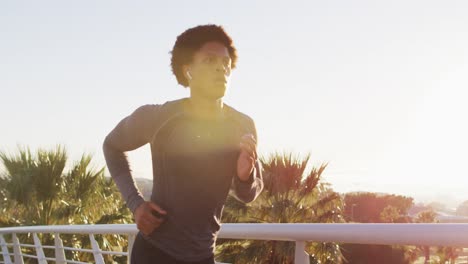 Fit-african-american-man-exercising-outdoors-in-city-wearing-earphones,-running-on-footbridge