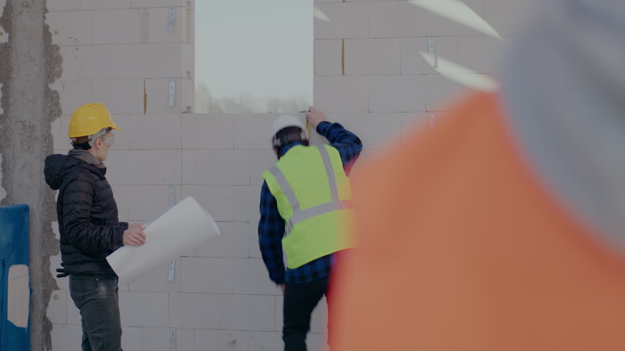 Young male construction worker measuring window frame while discussing with female architect holding blueprint at site