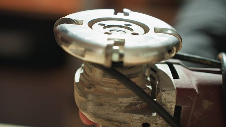 Close up shows detailed metal components of handheld angle grinder or similar rotary cutting tool. Hands adjust blade tension and alignment focusing on mechanical details like bolts bearings