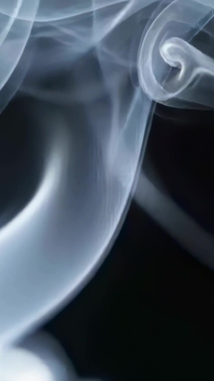 Vertical video: Rising from studio base ribboned smoke curling into spiral against black backdrop
