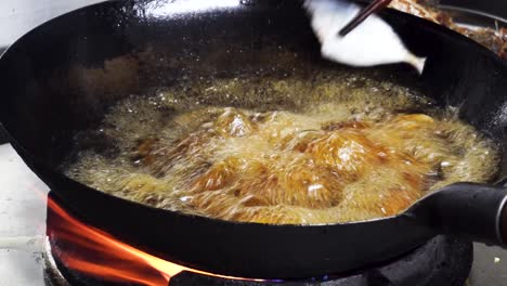 close up view fish head being deep fried in bubbling hot oil in saucepan