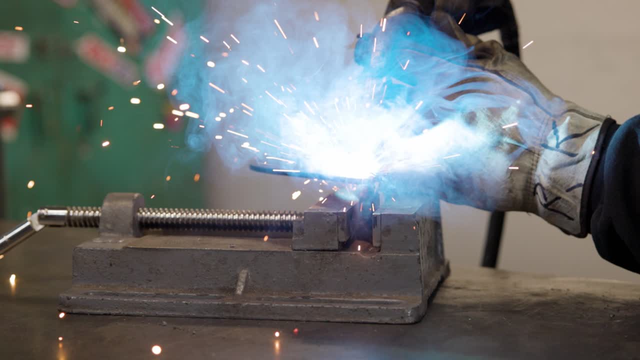 Close up of man mig welding bracket on a vise grip slow motion