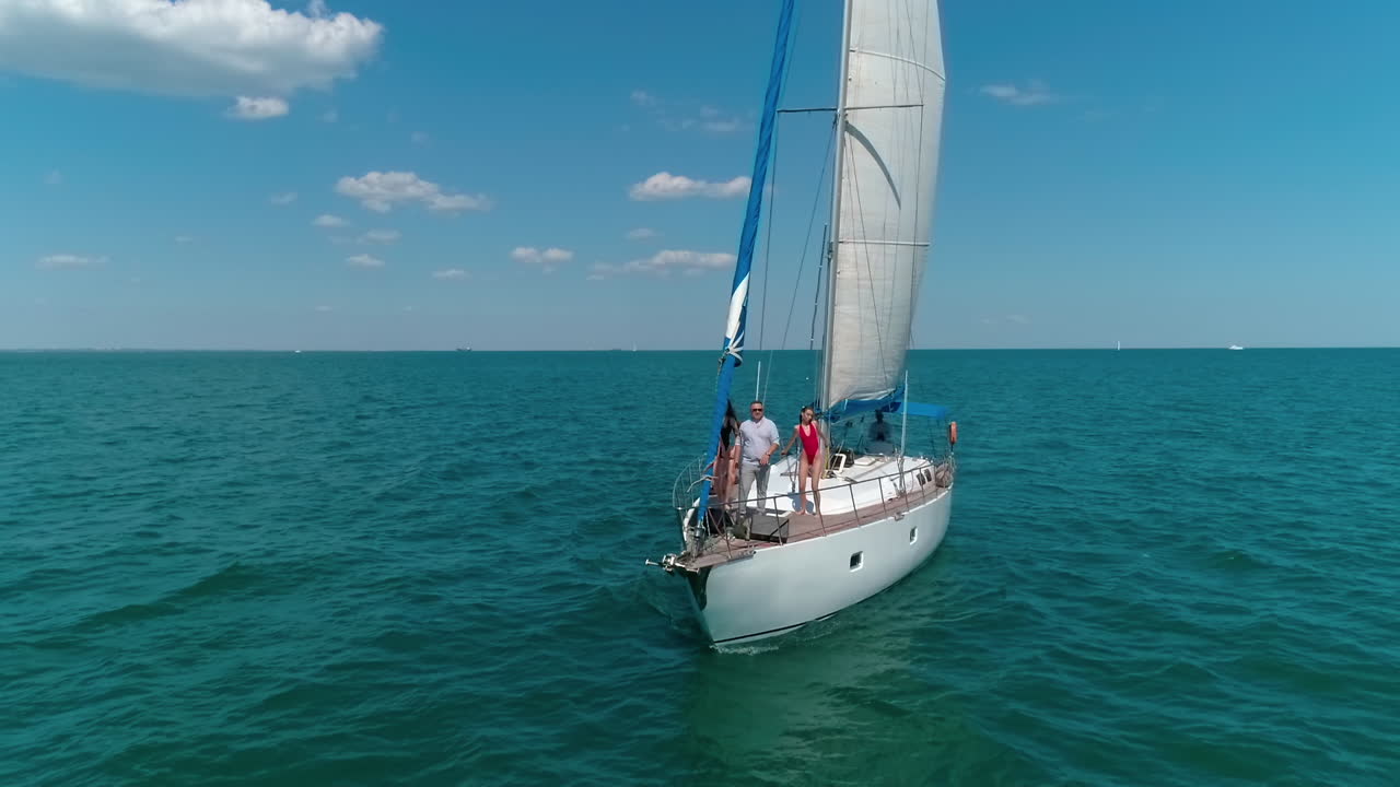Sea voyage on a yacht. Man and young women sing and dance on a sail boat in the open sea. People spend joyful time on a small ship in summer.