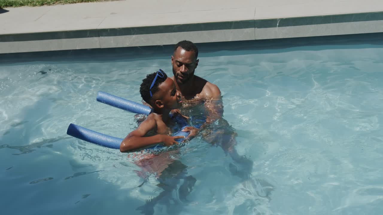 Guardião afro-americano sem camisa e criança aprendendo a nadar na piscina de casa, colocando boias de espuma