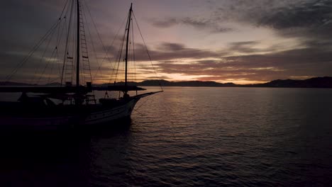 Silhouetted-boat-near-coastline-of-Langkawi,-Malaysia-at-sunset,-drone-flyby