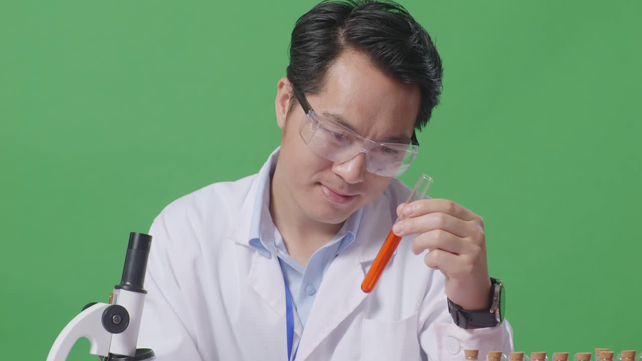 Close Up Of Asian Man Scientist Looking At Test Tube Then Smiling And Showing Thumbs Up Gesture While Working On The Table With Microscope In The Green Screen Background Laboratory