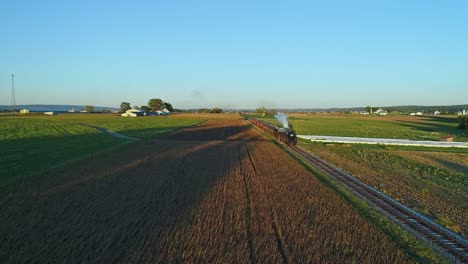 a drone view of an antique steam passenger train blowing smoke and steam traveling thru fertile corn fields during the golden hour in slow motion on a sunny summer day