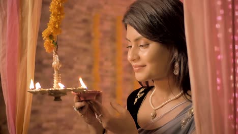 a slow mo shot of  happy female in a traditional clothing lights a hanging metal lamp in a house decorated with lights and flowers