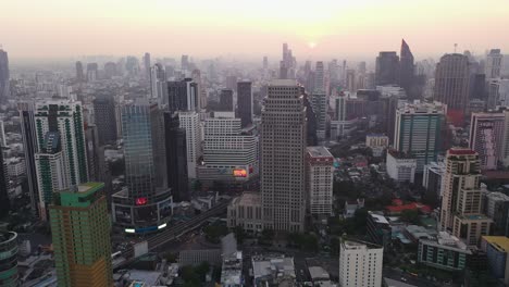 drone descending over skyline, buildings and skyscrapers of sukhumvit district during colorful warm sunrise in bangkok, thailand.