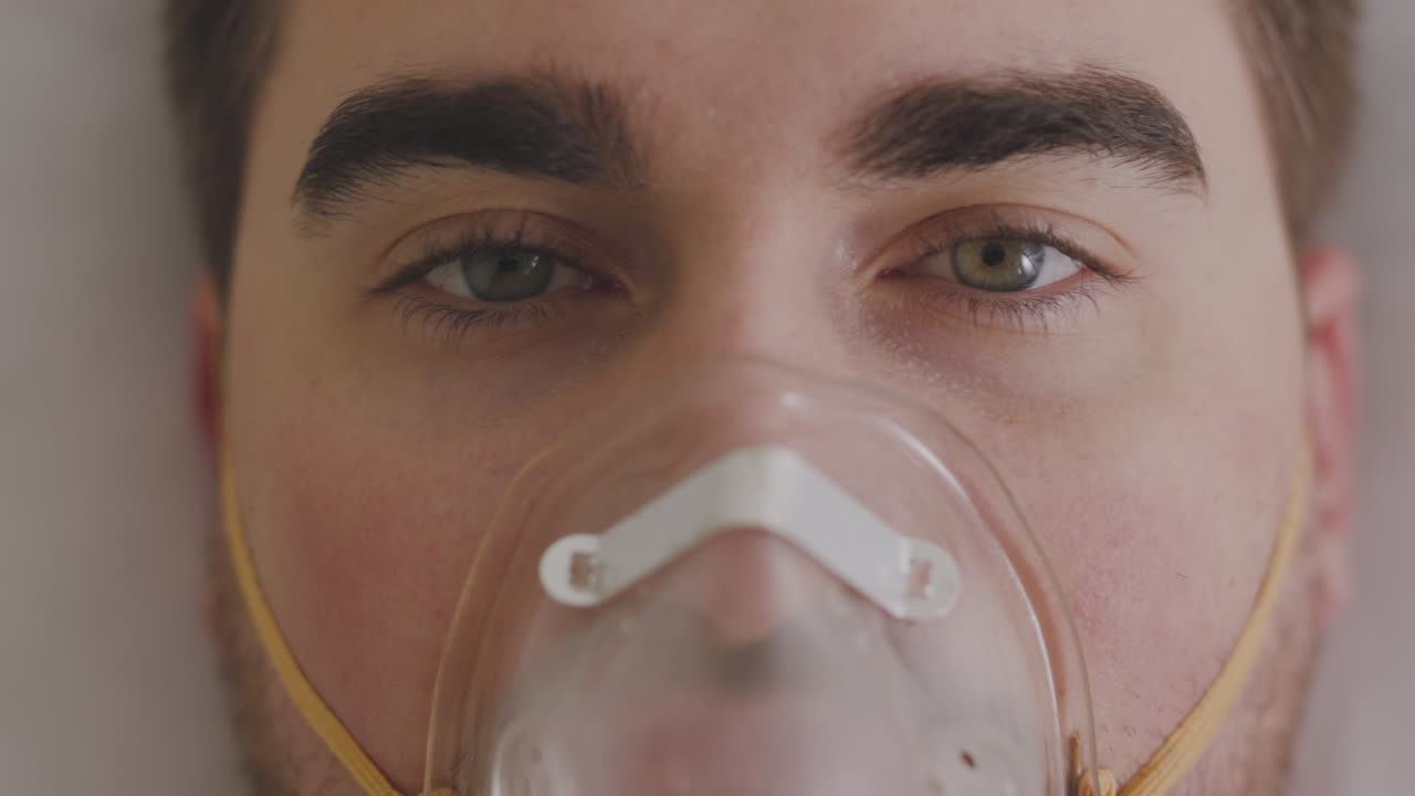 primer plano de un hombre enfermo que respira a través de una máscara de oxígeno y mira la cámara 1