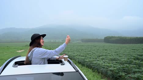 asian woman standing out of car sunroof. relaxing and freedom with spring time. young tourist travel alone in thailand on summer holiday.