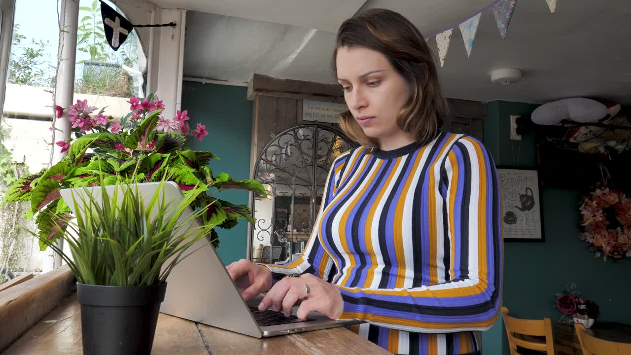 Young digital nomad focused on working on a laptop in a charming village café, epitomizing the blend of technology and traditional ambiance