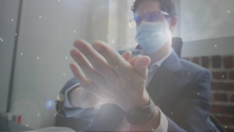puntos de luz contra el hombre caucásico que usa una máscara facial usando desinfectante de manos en la oficina
