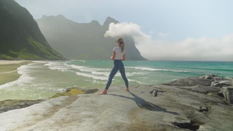 yoga warrior pose done by attractive woman on coastline of norway