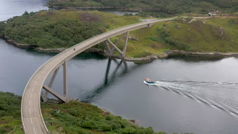 Rotierende-Drohnenaufnahme-Der-Kylesku-Brücke-Mit-Einem-Boot,-Das-Unter-Der-Brücke-Durchfährt,-Im-Nordwesten-Schottlands,-Das-Den-Loch-A&#39;-Chàirn-Bhàin-In-Sutherland-überquert