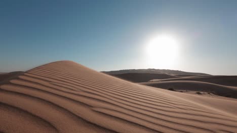 una duna de arena texturizada con un patrón barrido por el viento en la parte superior cuando el sol brillante comienza a descender a lo largo del horizonte