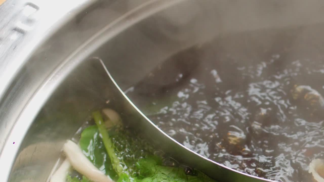 Thinly sliced meat is dipped into a steaming, bubbling dark broth within a divided pot