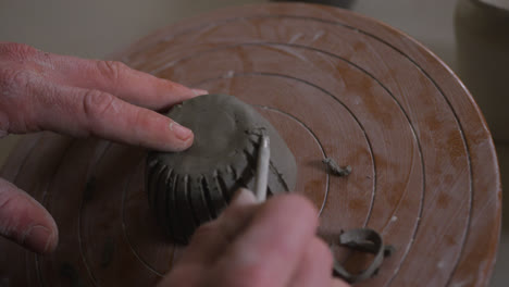 Close-up-view-of-male-potter-using-ribbon-tool-to-create-design-on-pot-at-pottery-studio