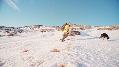 young man with backpack and alaskan malamute dog climb on the snowy mountain on a sunny winter day in norway