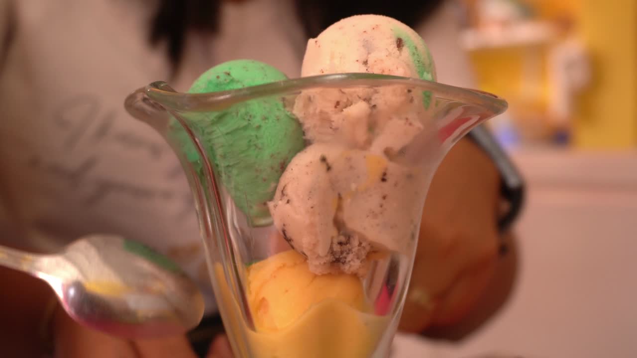 primo piano di varie palle di gelato verdi, gialle, rosse e bianche in una tazza di vetro a