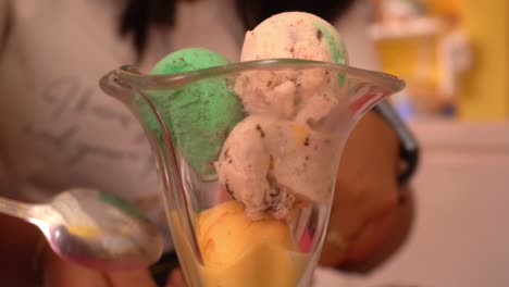 closeup of various green, yellow, red and white ice cream balls in a glass cup a