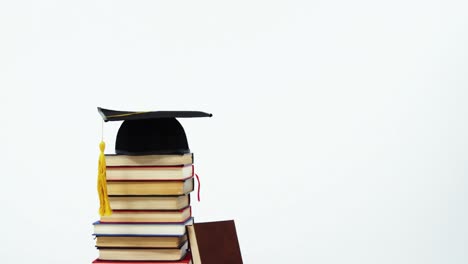 Close-up-of-mortar-board-and-stack-of-books