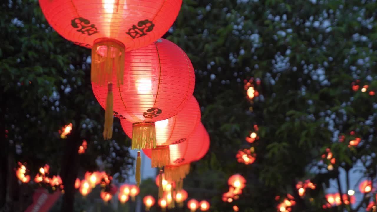 Red Chinese lanterns glowing at dusk during festival, hanging outdoors with trees in background