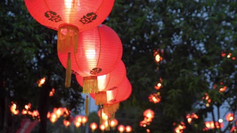 red chinese lanterns glowing at dusk during festival, hanging outdoors with trees in background