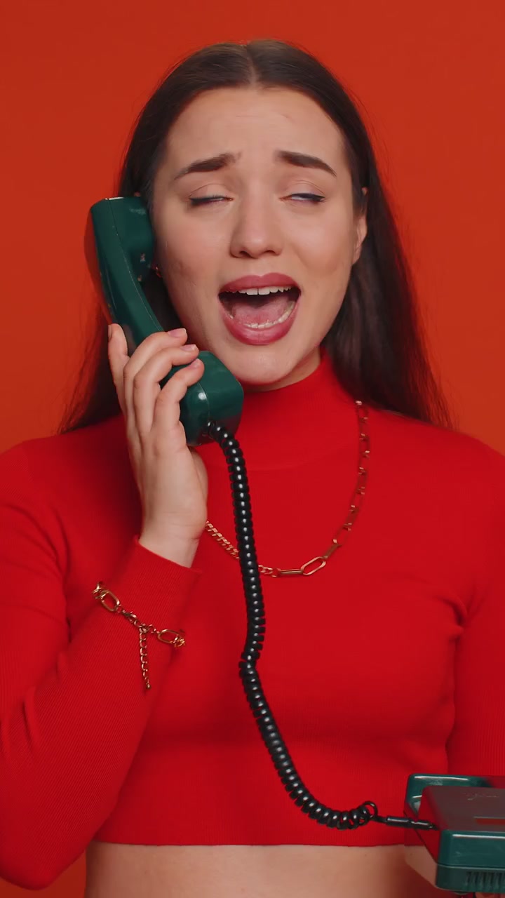 Donna annoiata e stanca che parla al telefono fisso vintage, facendo facce buffe durante una conversazione spiacevole.