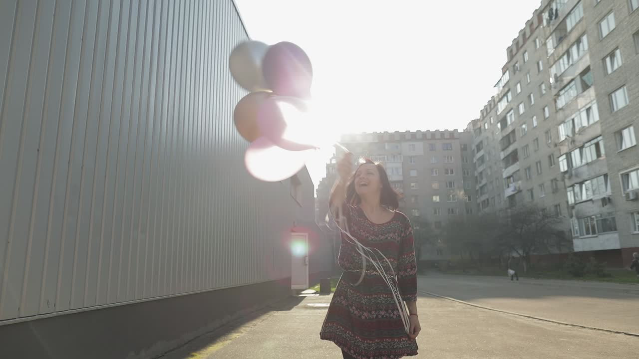mujer bonita en vestido sosteniendo globos con helio al aire libre a la luz del día