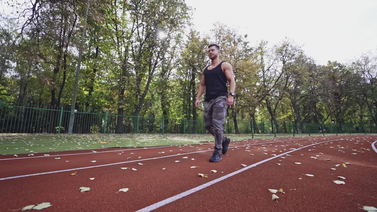 Healthy athlete walking on the modern stadium. Handsome sportsman lifting heavy weights on the nature background. Slow motion.