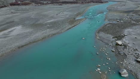 aerial view of tranquil scene of a turquoise river winding through a mountain valley with overcast skies and snow-capped peaks