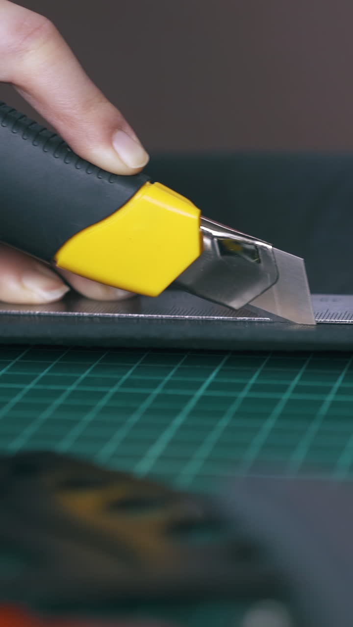 CU: Careful tailor cuts black leather cloth with special yellow box cutter holding metal ruler in hand closeup
