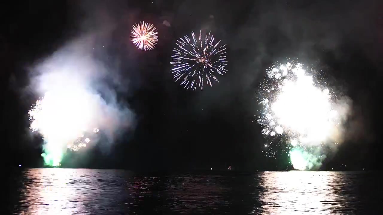 暗い海の上空で打ち上がり、水面に光を反射させる鮮やかな花火。