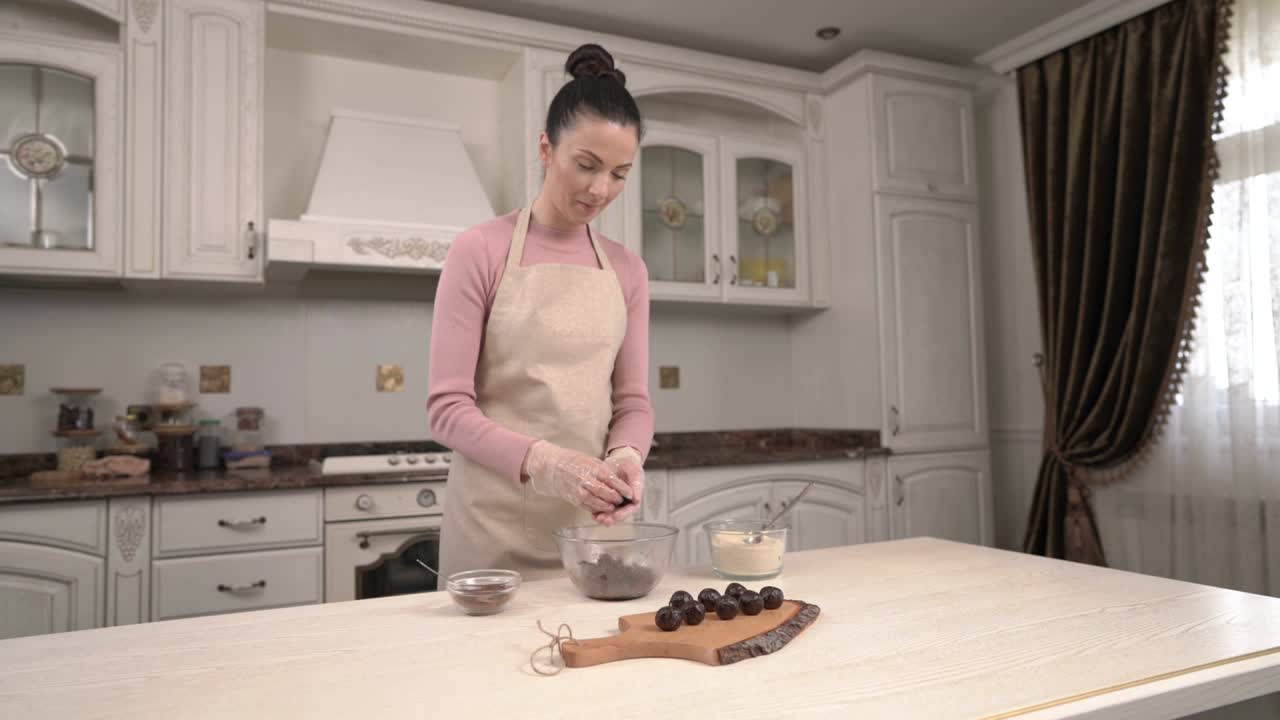 Giovane donna caucasica in una splendida cucina interna prepara cioccolatini e li posiziona su un tagliere di legno. Video dimostrativo ricetta dolci fatti in casa