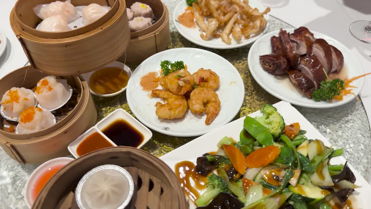 A vibrant display of dim sum and Chinese dishes on a lazy Susan, featuring dumplings, shrimp, and roast duck