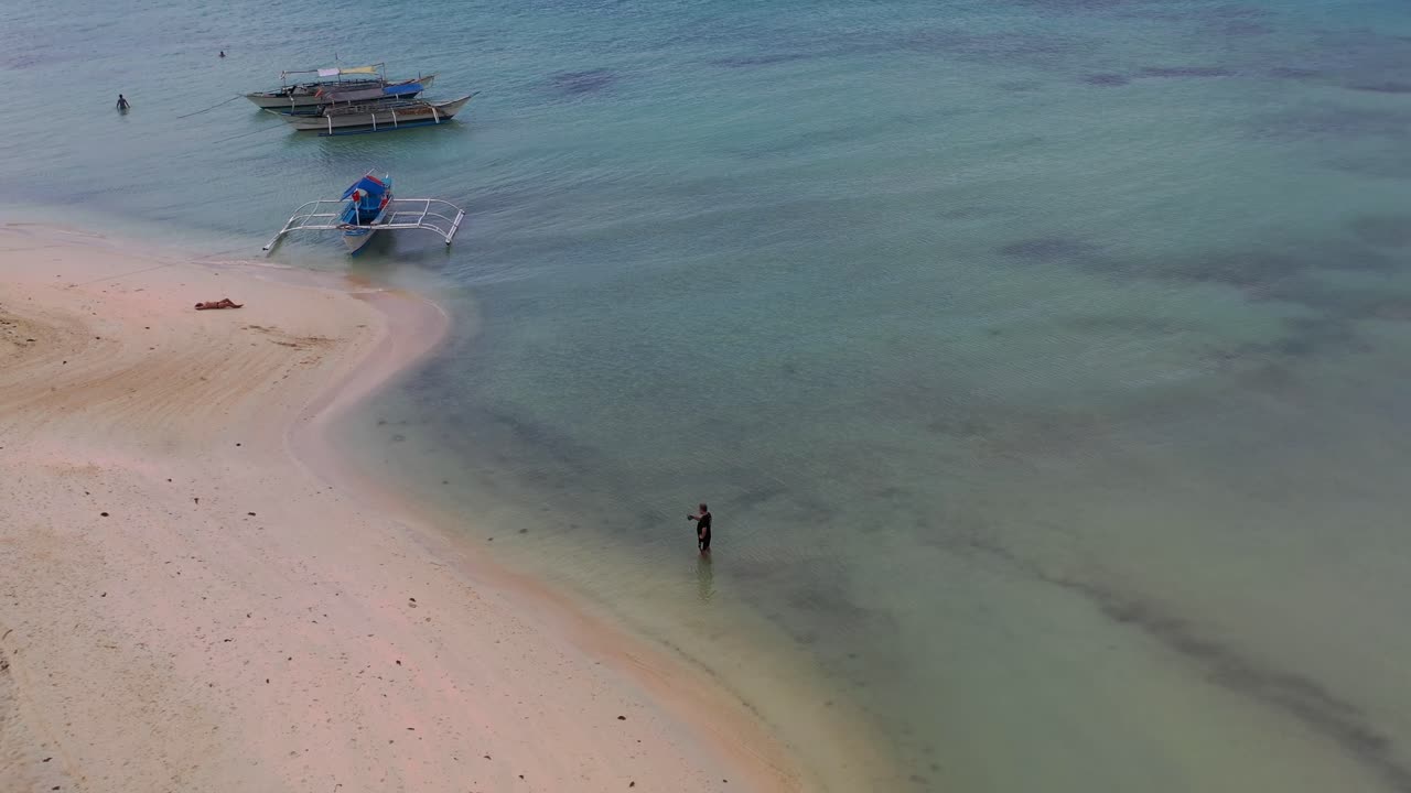 バンタヤン島フィリピンのコタ・ビーチ。浅瀬のビーチで男性がドローンを飛ばし、周りを旋回している様子。