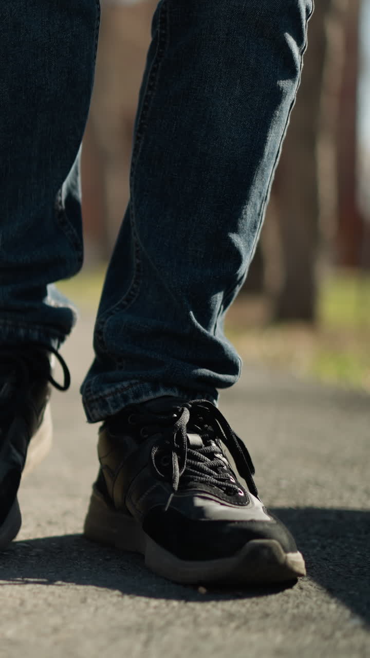 A close-up of an adult and a child wearing jeans and boots walking together on a pavement, the child is walking in an irregular pattern, with blurred view of house around